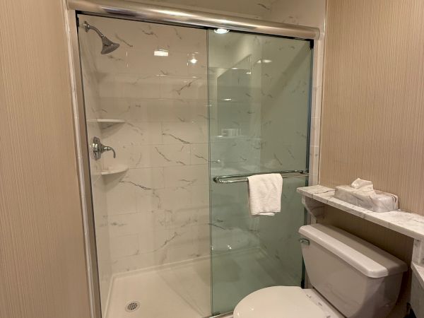 A modern bathroom with a glass shower, marble-look tiles, a towel on the rail, and a toilet in view.